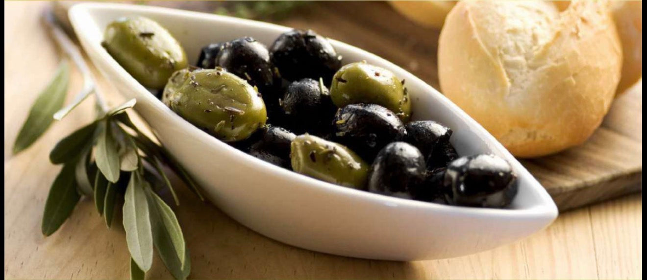  Bowl of mixed green and black olives with herbs, served beside fresh bread and olive branches on a wooden table