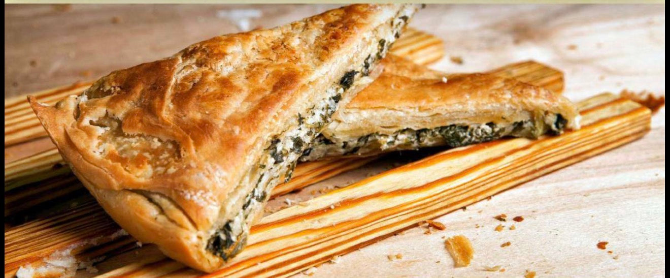 Flaky spinach and cheese pastry slices on wooden serving boards, with golden brown crust and visible layered filling.