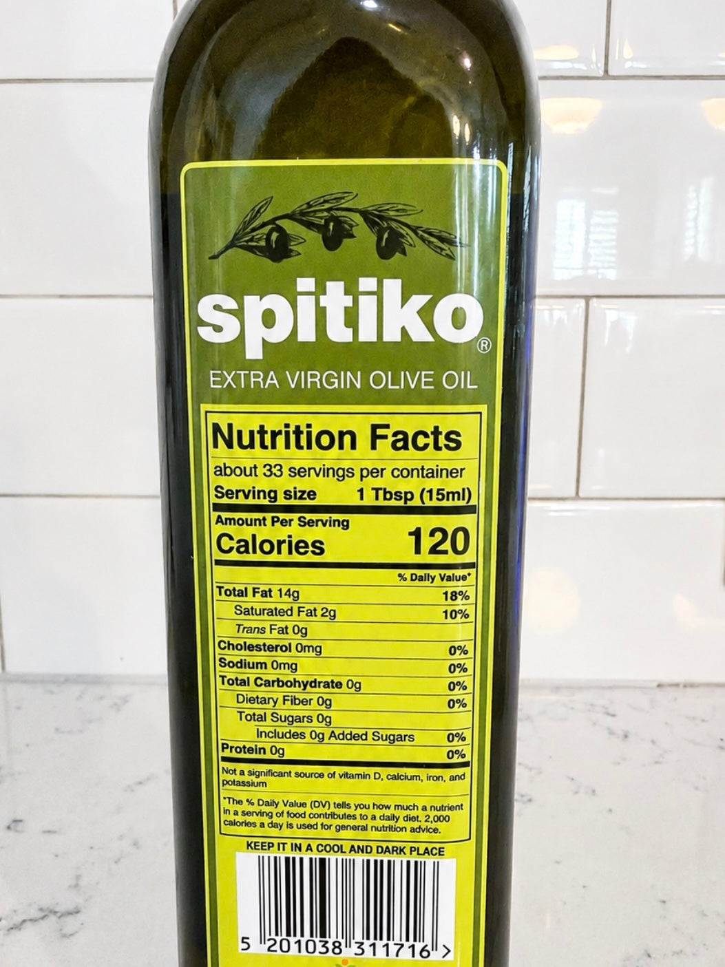 Bottle of Spitiko Extra Virgin Olive Oil with nutrition facts label on a tiled wall background